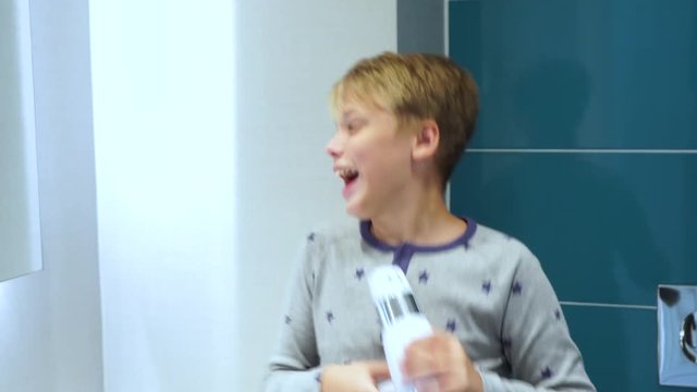 Portrait of cute handsome little kid dressed in pyjama singing and cheerfully dancing in bathroom. Boy uses hairdryer as microphone. Real time 4k video footage.
