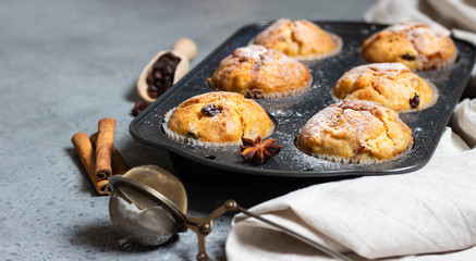 Fresh homemade apple cinnamon muffins in black baking dish with raisins, cinnamon sticks and anise.
