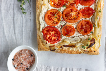 Deliciously simple tomato tart, puff pastry topped with cream cheese or ricotta and tomatoes on parchment paper. Summer tart. Top view. Copy space