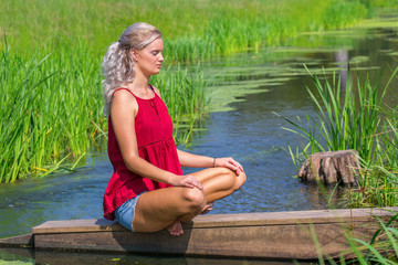Young blond woman meditating at water in nature