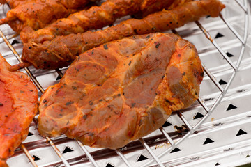 rohes Fleisch auf einem Grillrost und einer Aluminium Auffangschale / Grillschale
