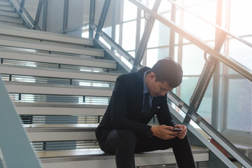 Young asian businessman sitting on stairs are stressing when he know business is failing and unemployed.