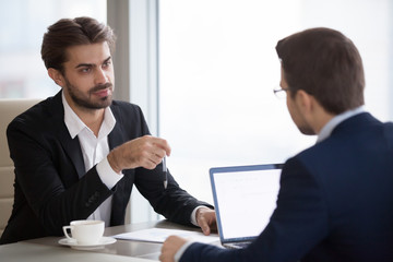 Fototapeta premium Two men in suits talking in office. Team members or colleagues or manager and subordinate discussing something at table, coaching, consulting. Process of results assessment or negotiation