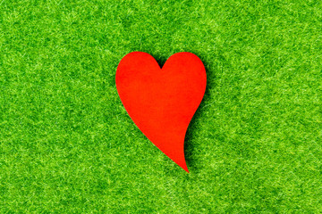 Red heart shape on green artificial grass background.