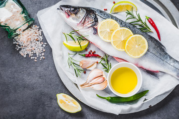 Fresh fish sea bass and ingredients for cooking. Raw fish sea bass with spices and herbs on black slate table copy space.