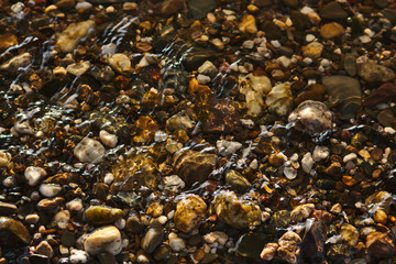 Schöne Kieselsteine im Flussbett mit Lichtreflexen und leichten Wellen