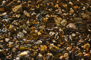 Schöne Kieselsteine im Flussbett mit Lichtreflexen und leichten Wellen
