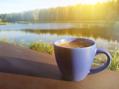 A cup of coffee by a lake in the morning. View from country homestead balcony