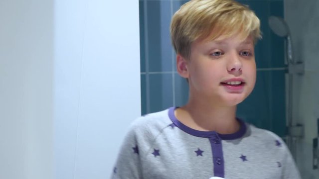 Cute white kid singing song and dancing happily before mirror in bathroom. Child holding hairdryer as mic. Real time 4k video footage.