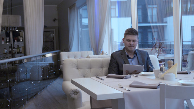Handsome guy (man) in a suit restaurant, gets a menu. Concept of: Menu, Orders, Waiter, Business, Beautiful atmosphere, Lifestyle.