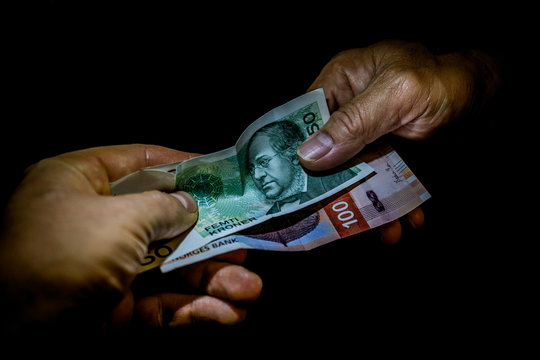 Two hands handing over Norwegian kroner banknotes to each other. Concept of tourist business profit, foreign investment, paying for the goods, shopping, money deal, banking or other financial service