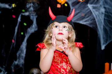 A child, a little girl in the shape of a witch on a broomstick, poses against the backdrop of scenery of cobwebs, pumpkins and autumn leaves on a Halloween holiday.
