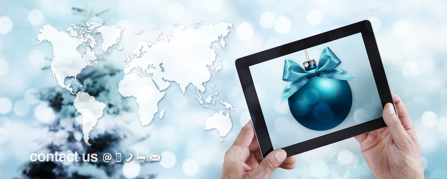 Christmas travel and online shopping concept, hands showing digital tablet with ball on blurred lights xmas tree and international map background, booking and contact us