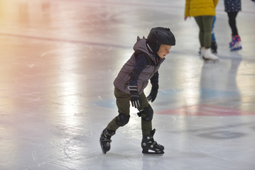 Fototapeta na wymiar Adorable little boy in winter clothes with protections skating on ice rink