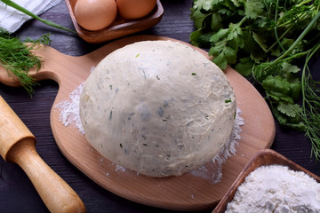 Yeast dough with herbs on a wooden board surrounded by the ingredients