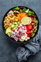 Healthy vegetarian Buddha bowl with fresh vegetable salad, rice, chickpea, avocado, sweet pepper, cucumber, carrot, pomegranate and nuts closeup