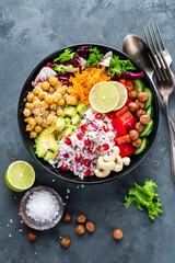 Healthy vegetarian Buddha bowl with fresh vegetable salad, rice, chickpea, avocado, sweet pepper, cucumber, carrot, pomegranate and nuts closeup