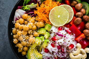 Healthy vegetarian Buddha bowl with fresh vegetable salad, rice, chickpea, avocado, sweet pepper, cucumber, carrot, pomegranate and nuts closeup