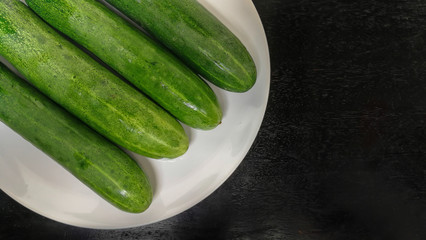 Fresh green cucumbers on white plate. Top view of wooden table. Copy space.