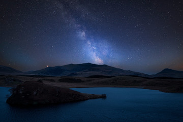 Vibrant Milky Way composite image over landscape of Llyn y Dywarchen lake in Snowdonia National Park - obrazy, fototapety, plakaty