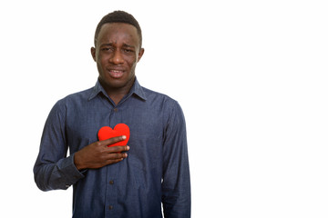 Young sad African man holding red heart on chest 
