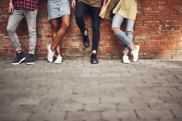 Relaxed young people standing next to the brick wall and putting feet on it while posing for a photo