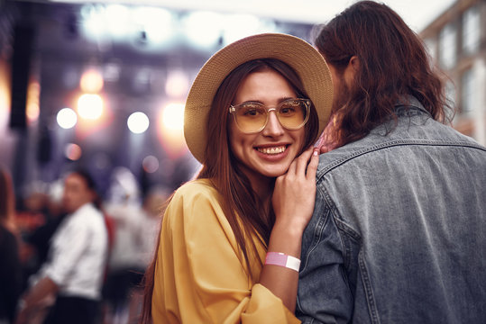 Portrait of charming young lady in hat standing close to hipster guy and looking at camera with smile