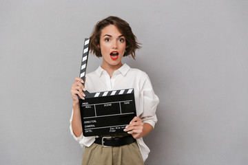 Photo of gorgeous woman 20s smiling and holding black clapperboard, isolated over gray background