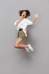Full length image of young girl 20s smiling and jumping, isolated over gray background
