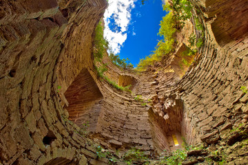 A look up from a medieval round stone tower without a roof, grass grows from the yellow walls, a blue sky with clouds. Koporye Fortress, Leningrad District, Saint Petersburg, Russia.