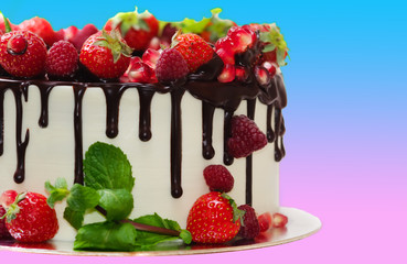 cake covered with berries of strawberry pomegranate raspberry mint leaves poured with chocolate on an isolated background with a gradient from blue to pink