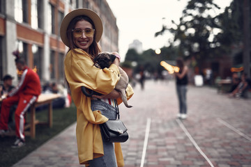 Portrait of stylish hipster girl in hat holding cute pug puppy and looking at camera with smile....