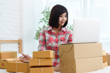 Woman small business owner, business start up in bedroom, young entrepreneur work with laptop prepare parcel boxes for deliver to customer