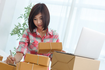 Woman small business owner, business start up in bedroom, young entrepreneur work with laptop prepare parcel boxes for deliver to customer