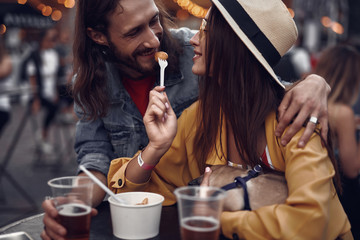Fototapeta na wymiar Portrait of young hipster couple enjoying company of each other in outdoor cafe. Lovely lady holding sleeping pug dog while bearded man staring at her with smile