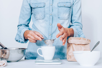 Female's hands sift flour it into measure cup