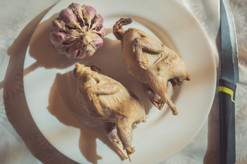 Two whole boiled quails, garlic and a knife lie on a white plate