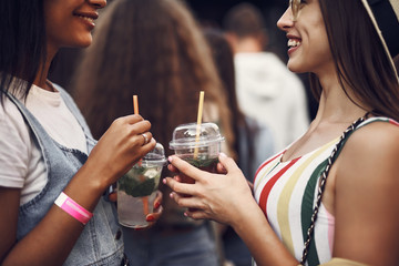 Cropped portrait of young smiling ladies holding drinks with mint. They looking at each other and smiling