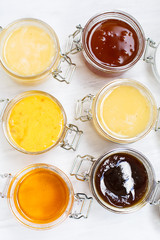 Jars with different kinds of honey in a row on a white wooden background