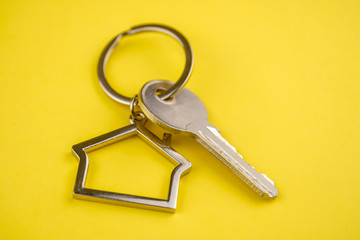 The concept of buying a private house or apartment. Metal keyring in the shape of a house with a metal key on a yellow background. Close up.