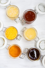 Jars with different kinds of honey in a row on a white wooden background