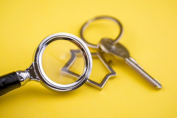 The concept of checking the legal purity of a private house or apartment. Metal keyring in the shape of a house with a metal key under a magnifying glass on a yellow background. Close up.