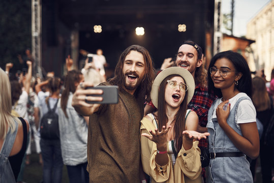 Waist up portrait of young people taking photo with smartphone. They enjoying concert and smiling