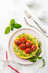 Frittata with arugula, potatoes and cherry tomatoes in iron pan on old stone table background. Top view.