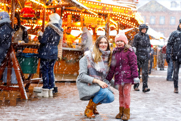 Little cute kid girl and young mother having fun on traditional German Christmas market during strong snowfall.