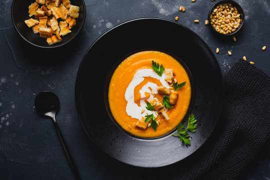 Pumpkin soup in black ceramic plate on dark wooden background. Traditional autumn food. Top view copy space.