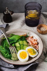 Scandinavian salad with smoked pink salmon, spinach, cucumber and chicken egg in gray ceramic dish. Top view.