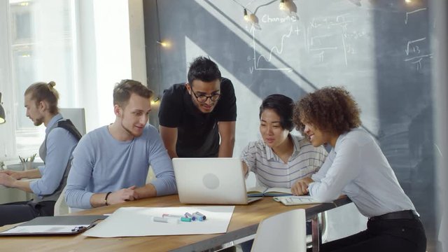 Group of multiethnic students or businesspeople sitting at desk and discussing something they see on laptop computer screen