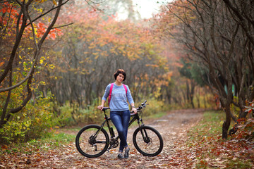 Plakat The girl on a bike from the rental in the forest. Beautiful young woman posing for the camera in the autumn forest. 