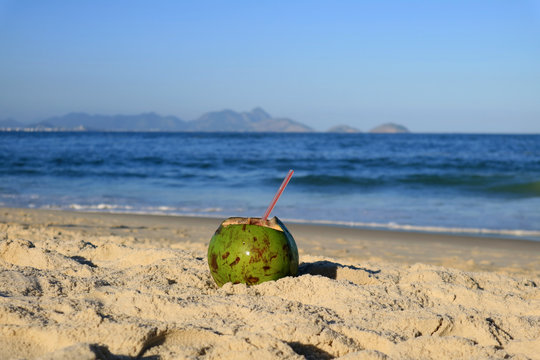 Fresh young coconut on the sandy beach Copacabana in Rio de Janeiro, with blurred Atlantic ocean in background 